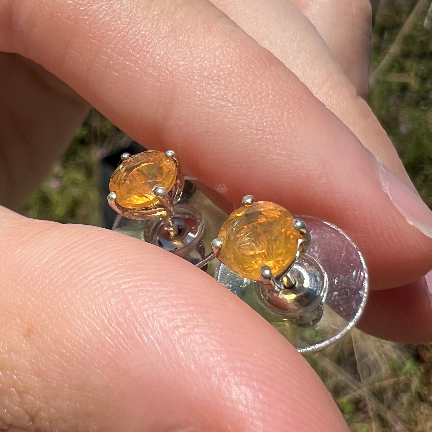 A pair of Mexican fire opal stud earrings in sterling silver held at an angle in sunlight.