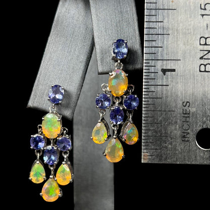 A pair of dangling sterling silver opal and tanzanite chandelier earrings next to a ruler, measuring 1.25 inches.