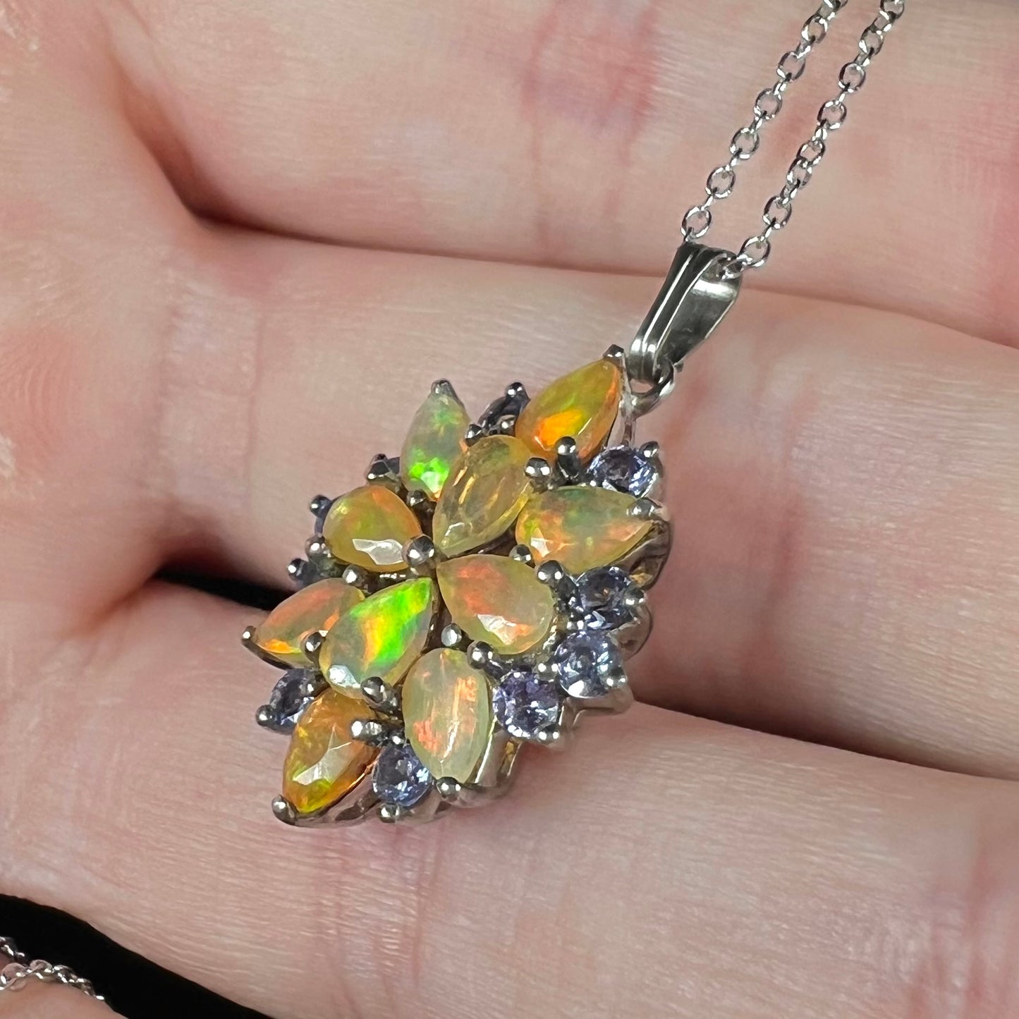 A sterling silver fire opal and tanzanite necklace shown close-up in a hand, held at an angle.