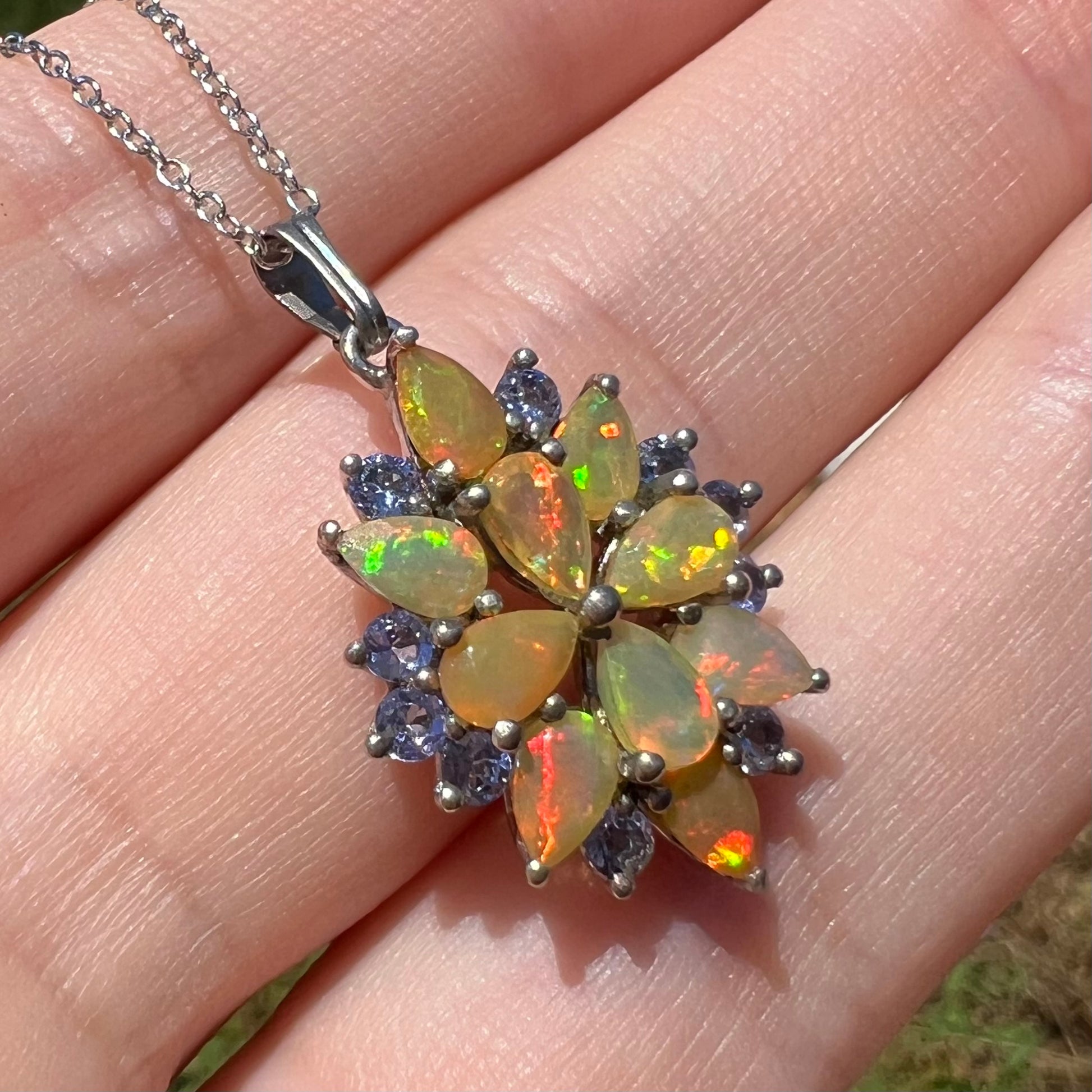 A fire opal and tanzanite custer pendant, shown in the sunlight at an angle.