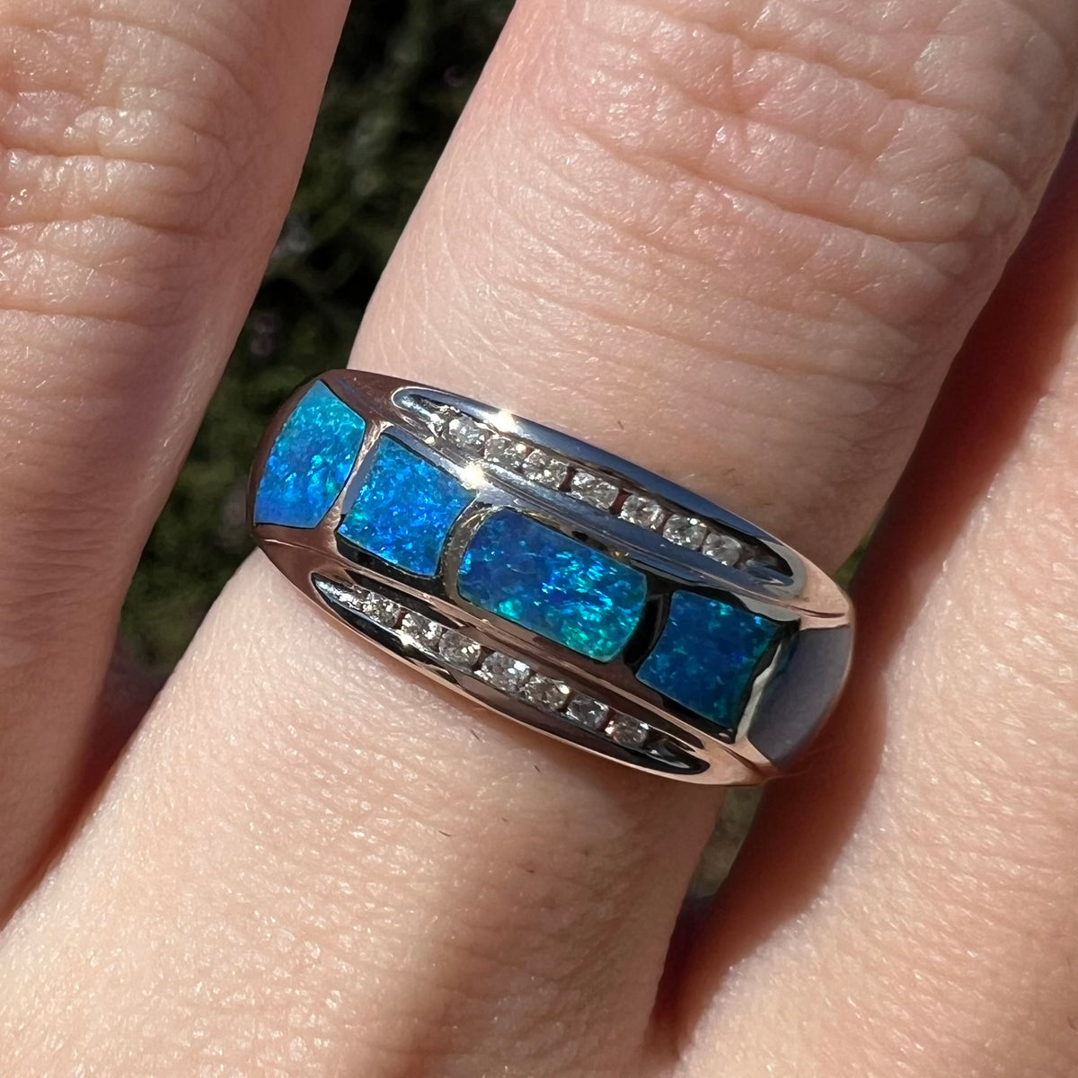 Close-up of five-stone opal inlay ring with diamond accents in 14k white gold, worn on finger in natural sunlight