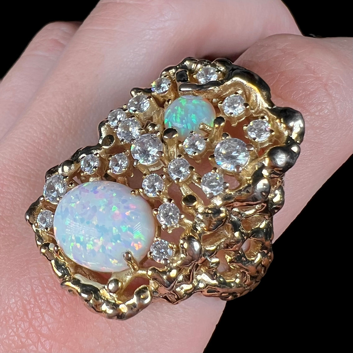 A large, flashy opal and cubic zirconia men's ring worn on finger and viewed from an angle.