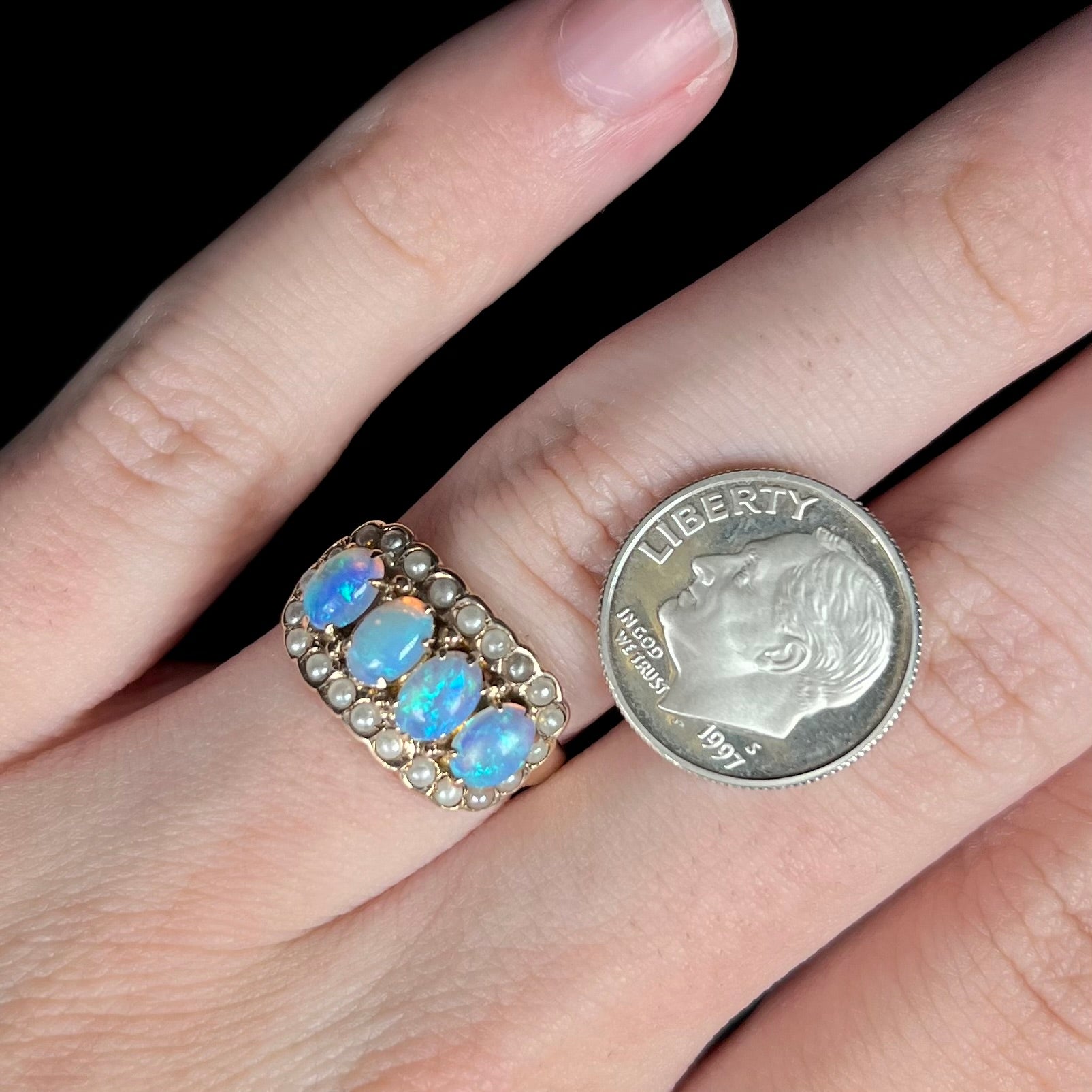 Close-up of hand wearing Victorian four-stone opal and seed pearl ring next to US dime coin