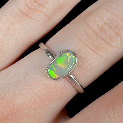 Macro view of a freeform-shaped Australian crystal opal bezel ring in sterling silver, shown on a finger.  The opal has green and orange flashes.