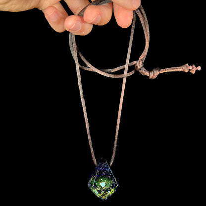 A galactic-inspired purple amethyst glass and lab-created opal necklace, dangled from its brown cord by a hand against a black backdrop.