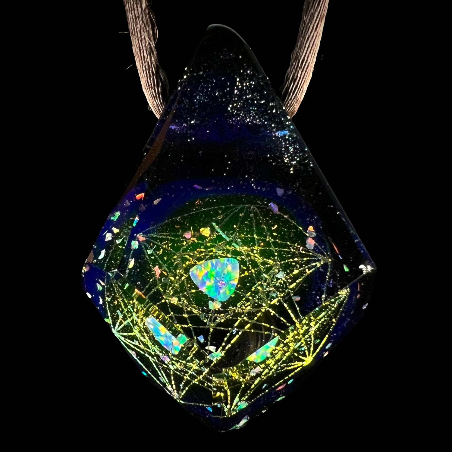 An opal in borosilicate glass pendant with a galactic-inspired motif by artist, Jes Durfee, shown close-up against a black background on a brown cord.