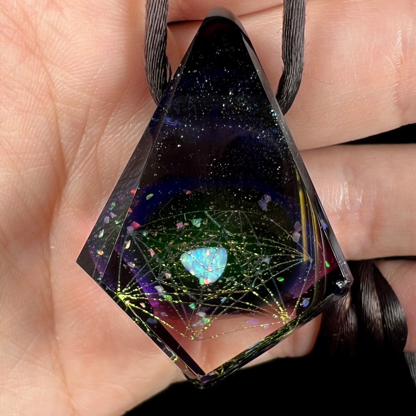 A purple glass and lab-created opal pendant with a galactic design, shown close-up in a hand.