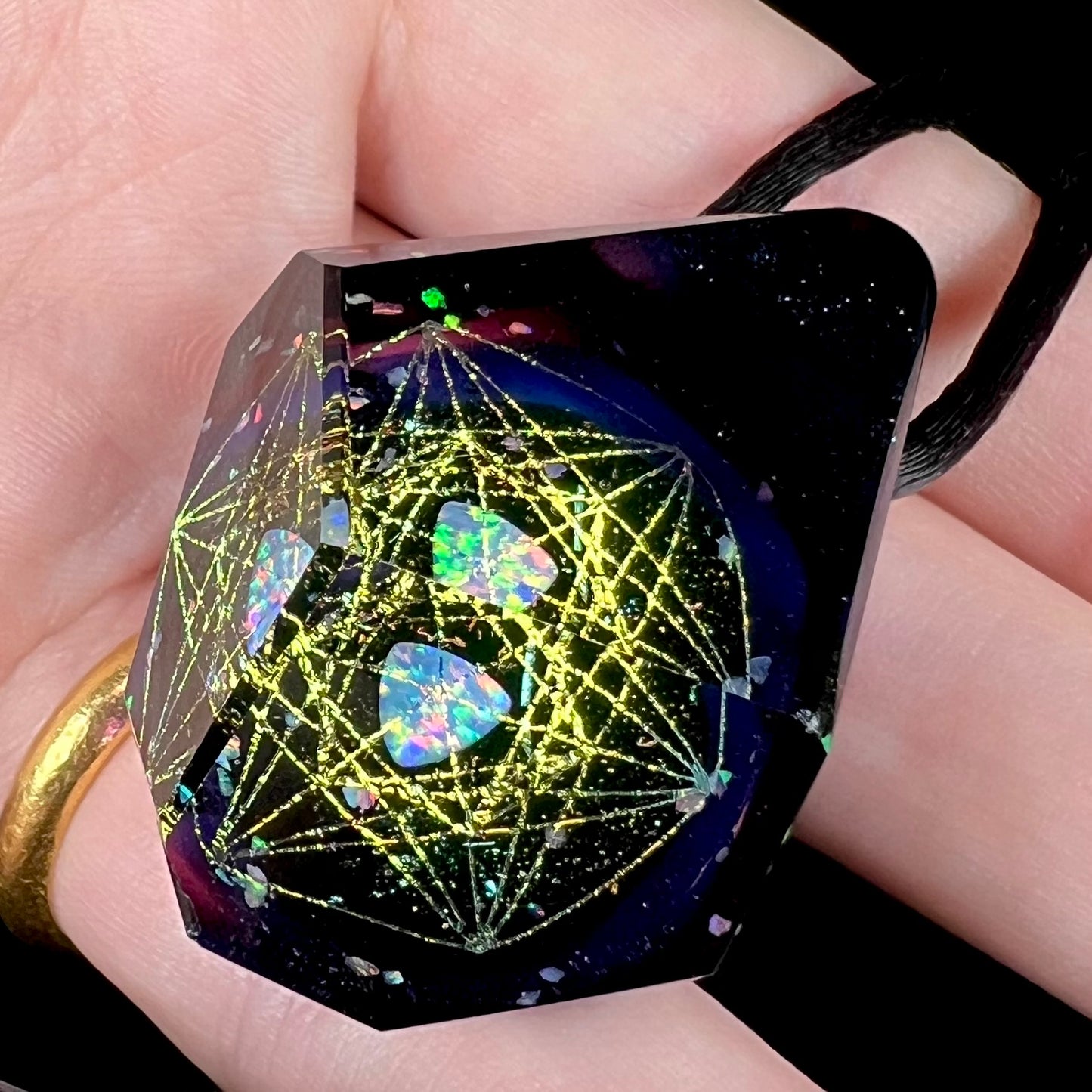 Angled view of a purple glass pendant featuring a galactic motif with sacred geometry and hexagram designs, shown close-up in a hand.