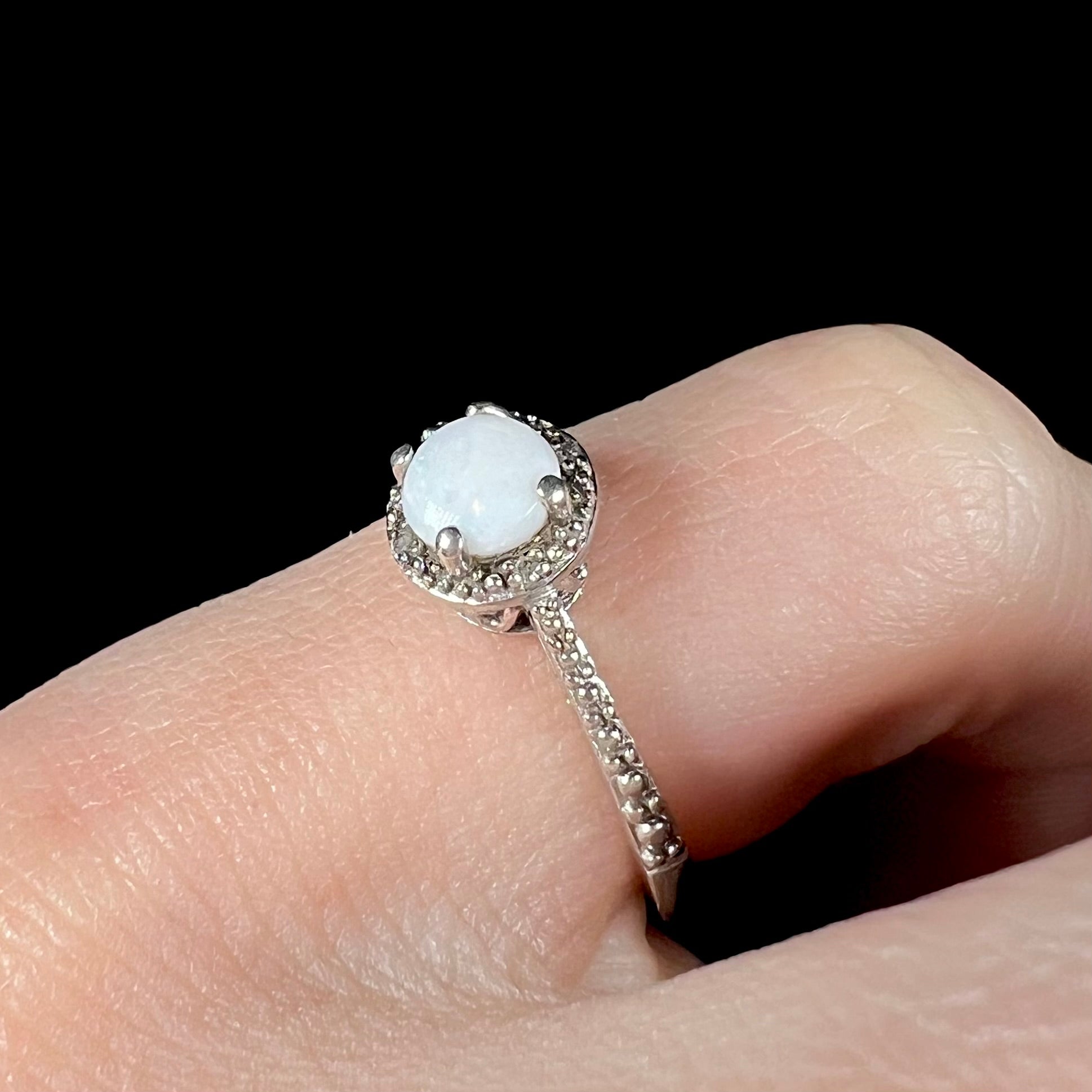 A sterling silver genuine opal and diamond ring with a halo design, worn on a pinky finger, shown at an angle.