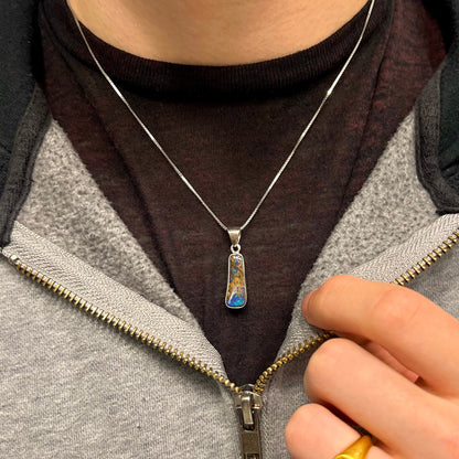 A sterling silver necklace bezel set with a natural Australian boulder opal stone.  The stone shines colors of blue, green, and purple.