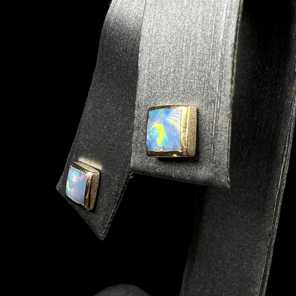 Angled view of geometric Australian opal stud earrings in 14k gold on earring display
