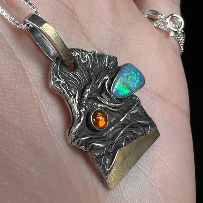 Angled macro view of a gold-accented sterling silver men's Australian opal doublet and amber pendant, held in a hand.