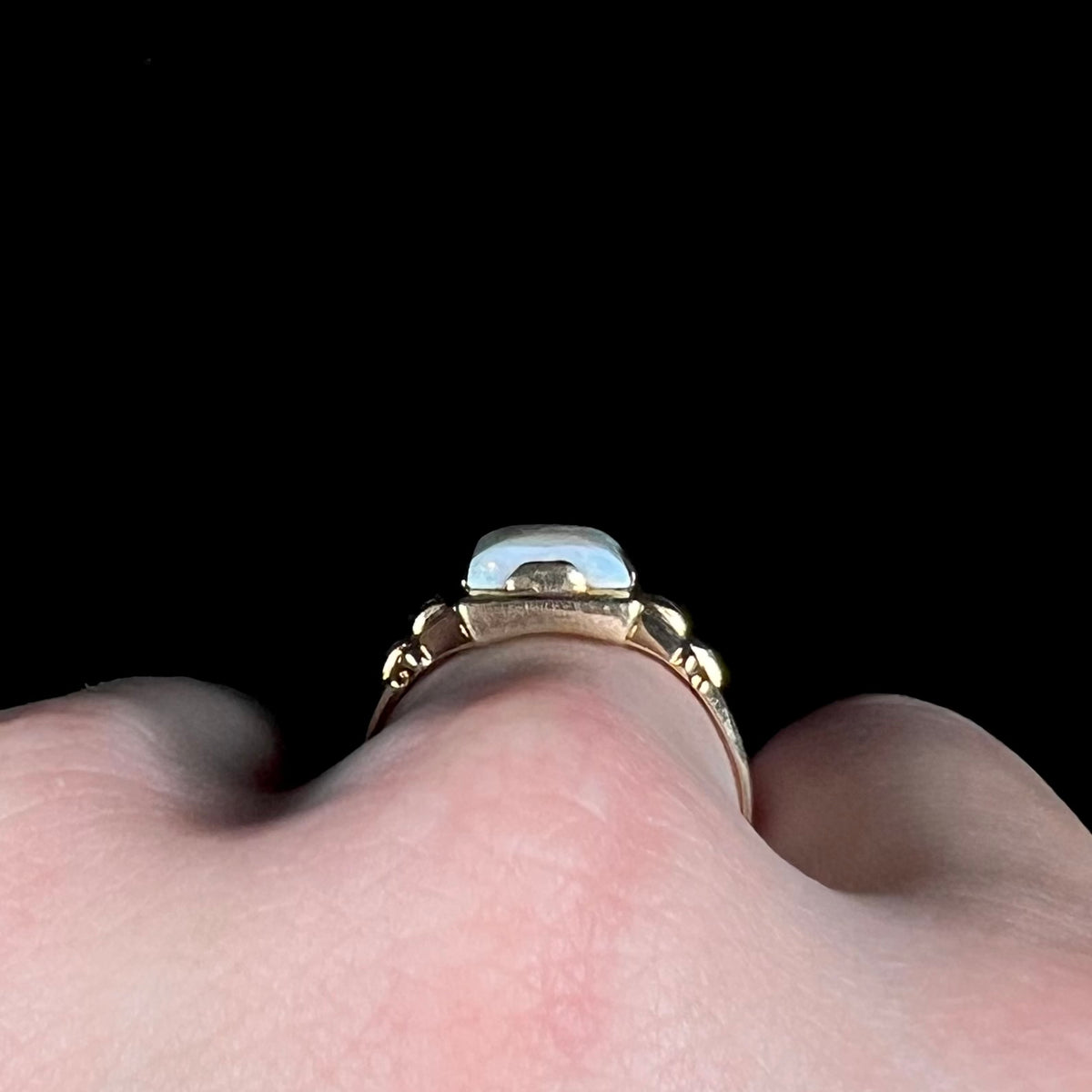 Side profile gallery view of a 10k gold Art Deco-style opal ring, worn on a finger; one of the ring's wide tab prongs is in view