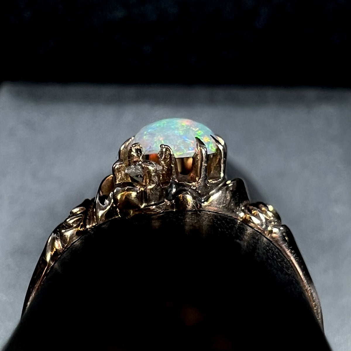 Side profile gallery view of a 10k gold Art Nouveau era opal and diamond ring, shown on ring display; a chip in the opal's edge is visible, as is damage to the prongs that hold it