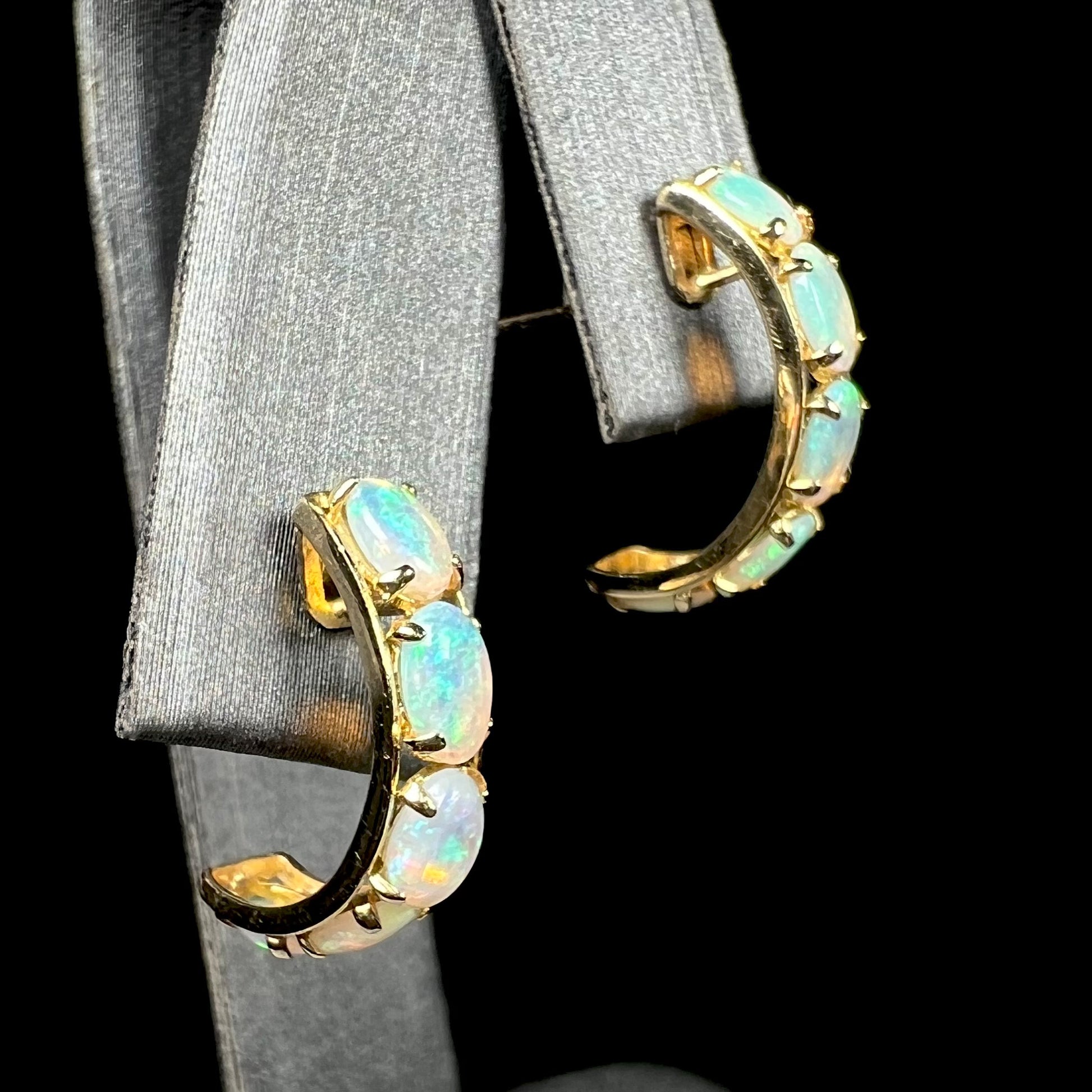 Pair of 14k gold Australian crystal opal hoop earrings shown close-up from an angle on an earring display against a black background.