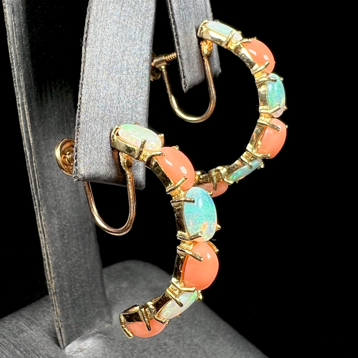 Angled side view of yellow gold Australian crystal opal and coral semi-hoop earrings, shown on earring display