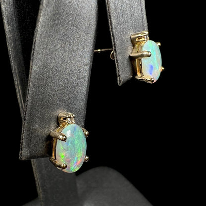 A pair of Australian crystal opal and diamond stud earrings in gold with green-blue color play shown from an angle on an earring display.