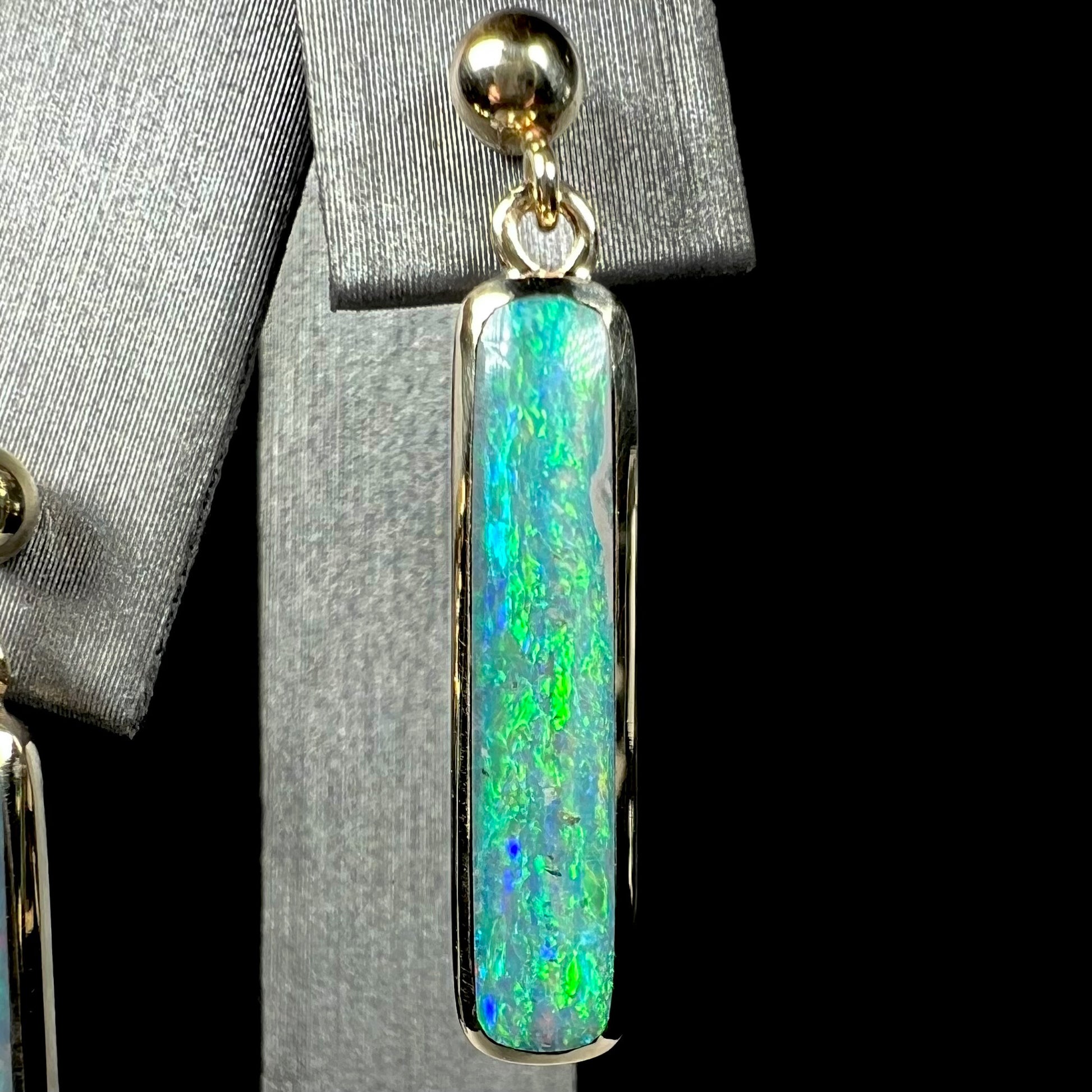 A single gold Australian opal drop earring with green fire, shown close-up against a black background.