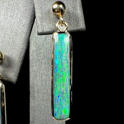 A single gold Australian opal drop earring with green fire, shown close-up against a black background.