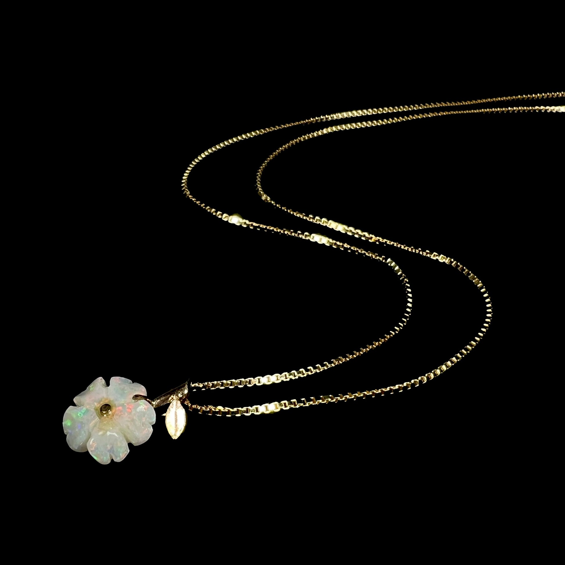 A gold carved Australian opal flower necklace shown from an angle laying on a black background.