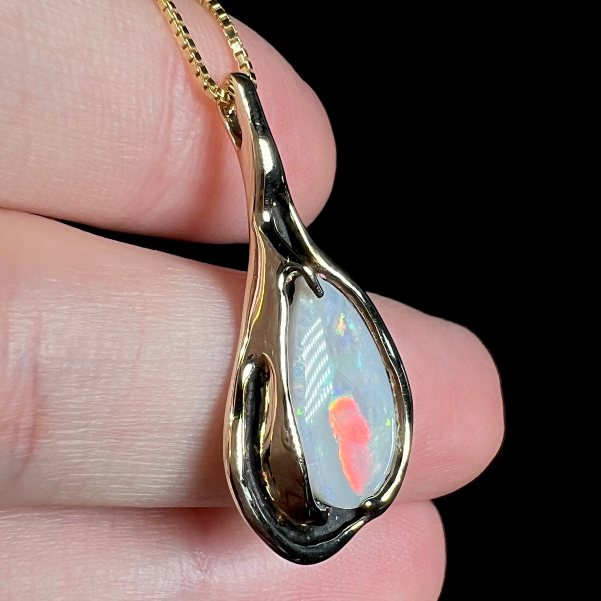 Red color bar lights up in 14k gold Australian opal pendant when viewed from side, held in hand