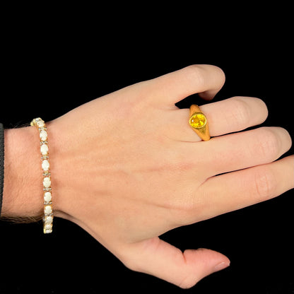 Hand wearing a gold Australian opal tennis bracelet around the wrist with a 24k gold yellow sapphire ring on the ring finger.