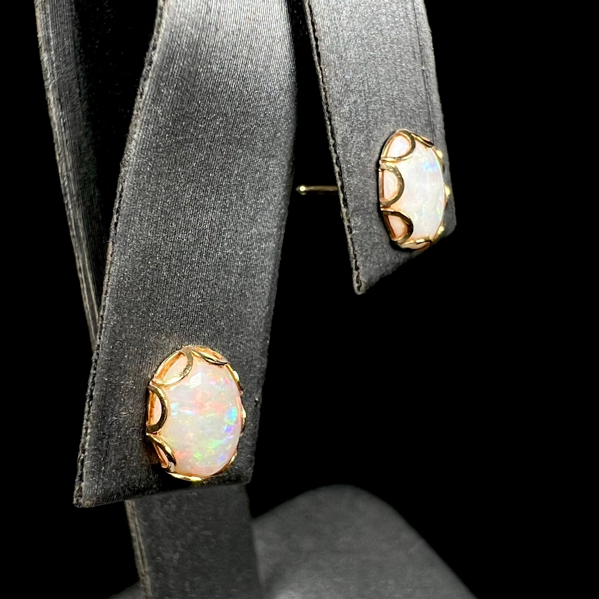 Angled view of a pair of Australian white opal stud earrings in yellow gold, shown on a ring display.