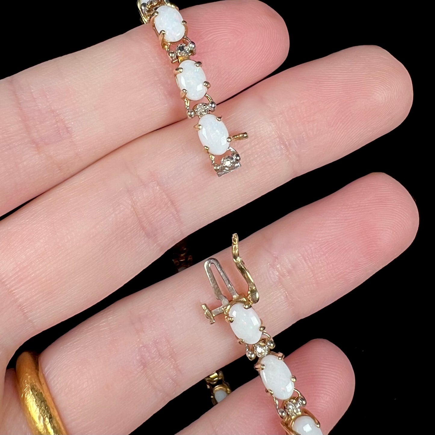 Hand holding a gold Australian opal tennis bracelet, showing its box clasp with a safety latch opened.