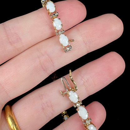 Hand holding a gold Australian opal tennis bracelet, showing its box clasp with a safety latch opened.