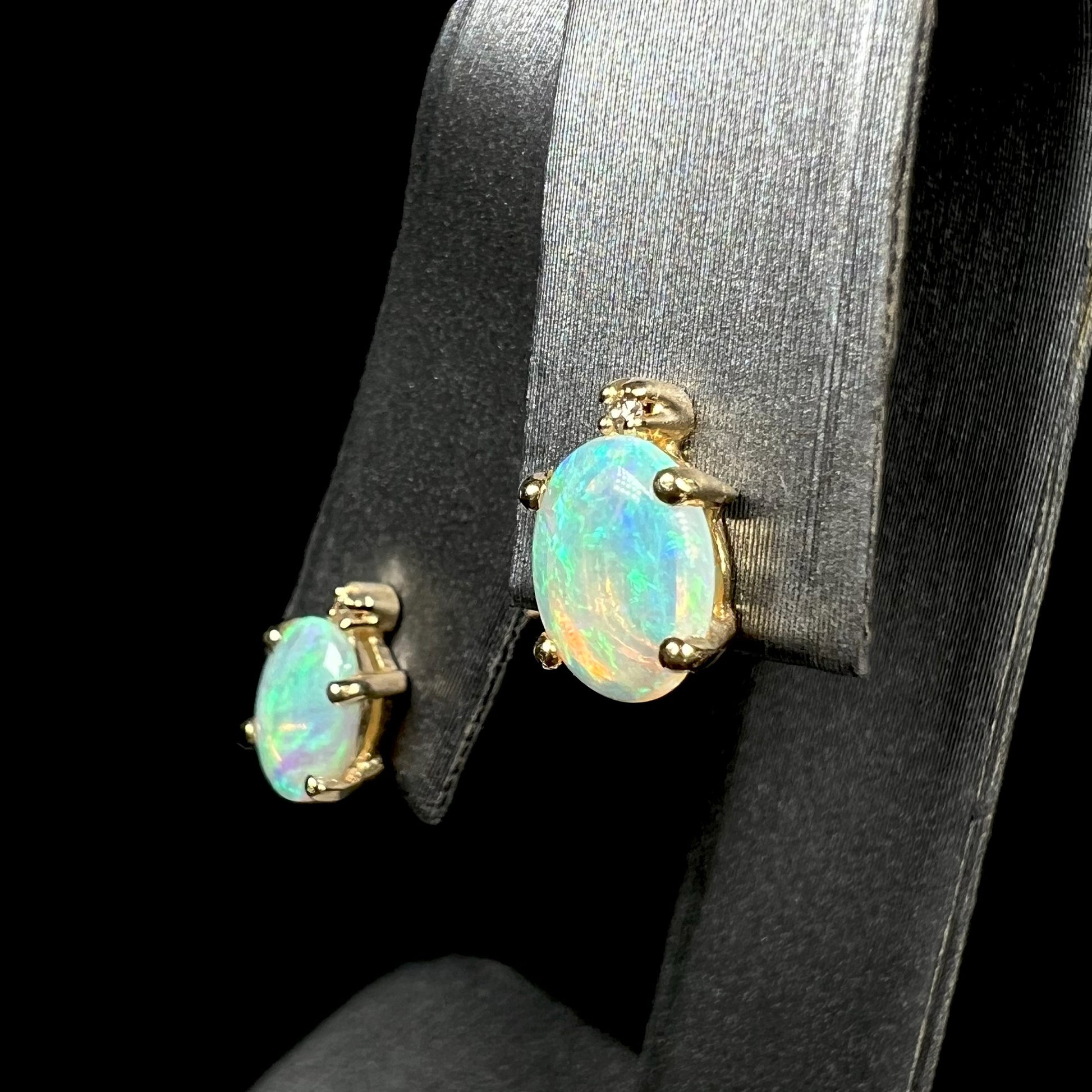 Angled view of a pair of Australian crystal opal and diamond stud earrings in gold with green-blue color play on an earring display.