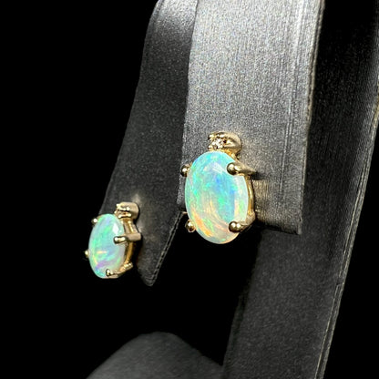 Angled view of a pair of Australian crystal opal and diamond stud earrings in gold with green-blue color play on an earring display.