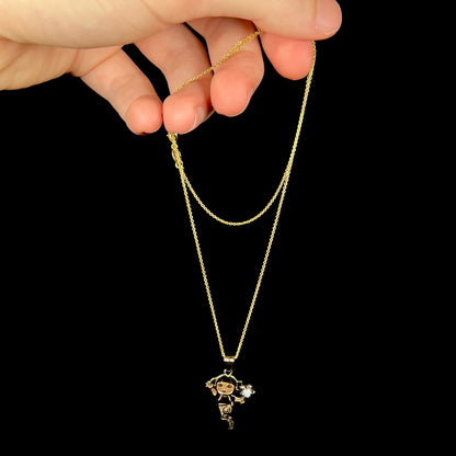 Gold-tone Dora the Explorer opal necklace dangled from its chain by a hand in front of black background.