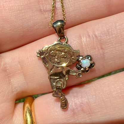 Close-up of gold Dora the Explorer opal pendant held in a hand under natural sunlight.  The opal has subtle pearlescent blue play of color.