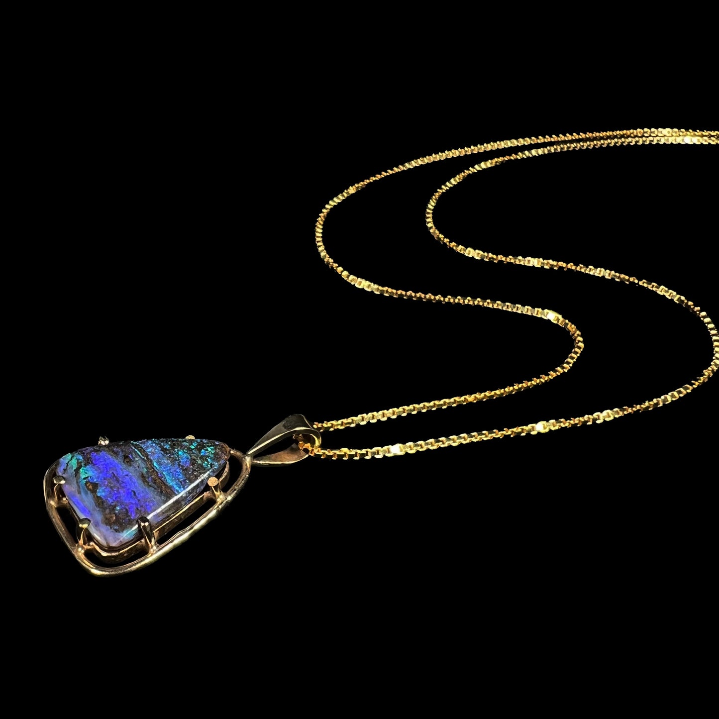 A dainty Duck Creek opalized wood necklace in 9k gold, shown from an angle laying against a black backdrop.