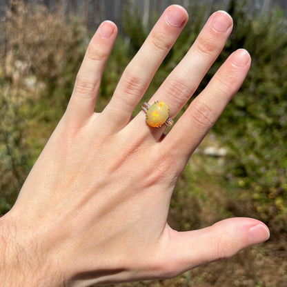 Hand wearing a 14k gold Ethiopian opal cocktail ring with diamond accents in natural sunlight