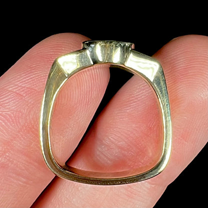 Fingers holding an 18k yellow gold unisex ring with a euro shank design, showing its side profile.