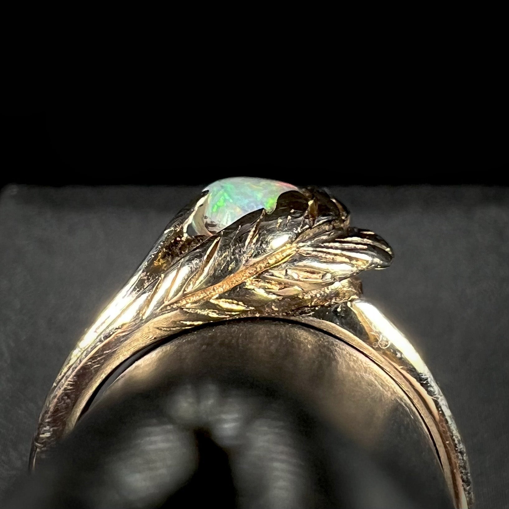 The gallery view of a retro, 1980's-style yellow gold feather ring mounted with a white opal.