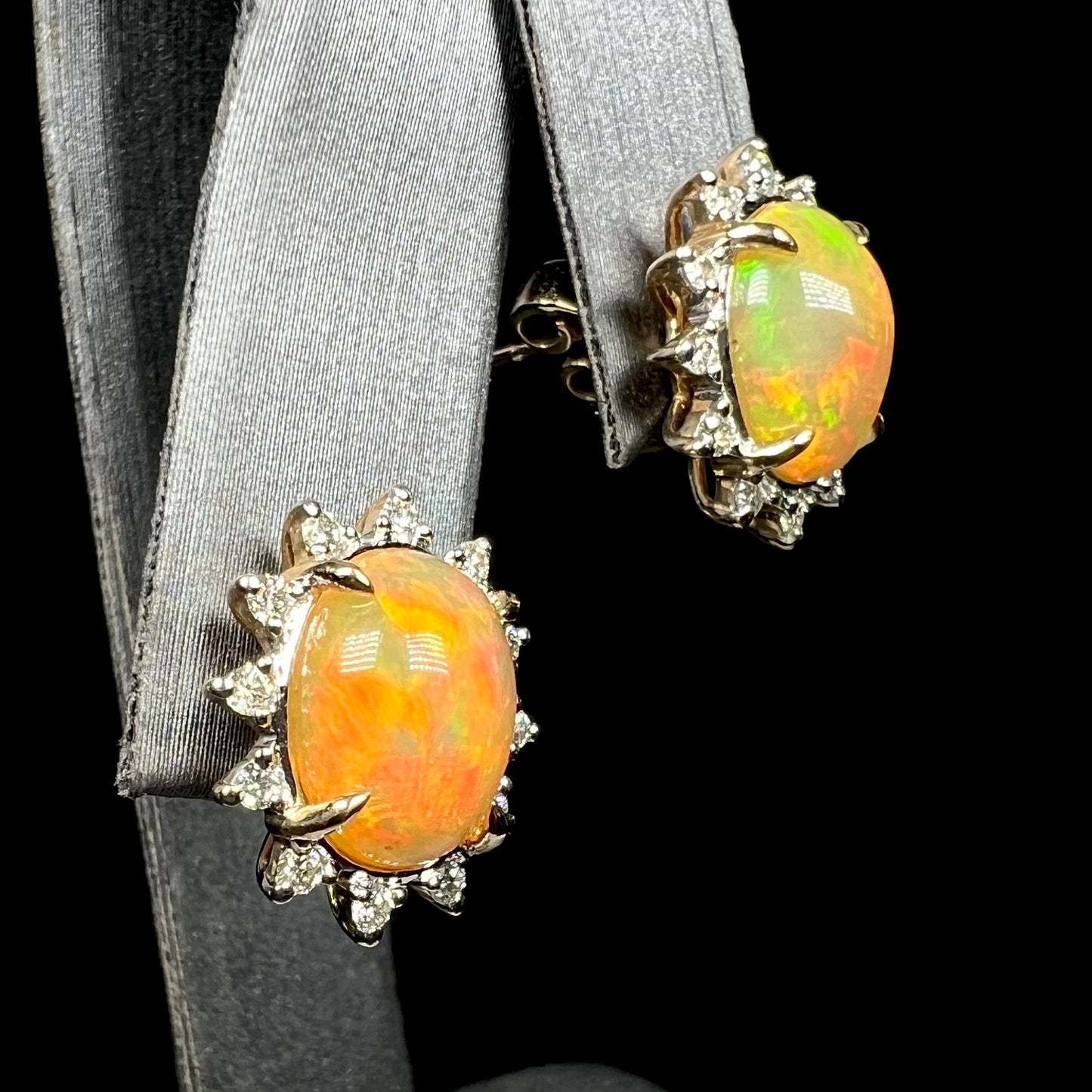 Pair of 14k gold fire opal and diamond halo stud earrings with red and green colors on earring display
