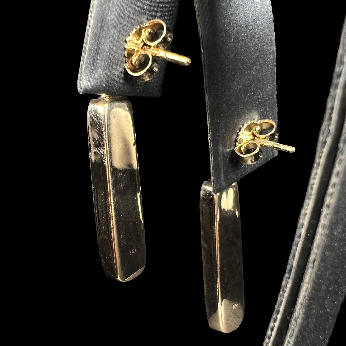 The solid back view of a pair of yellow gold inlay dangle earrings.  No stones are seen.