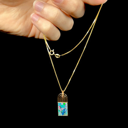 An 18k gold mosaic opal necklace being dangled by the chain in a hand, displaying red and green flashes across the individual opal inlays.