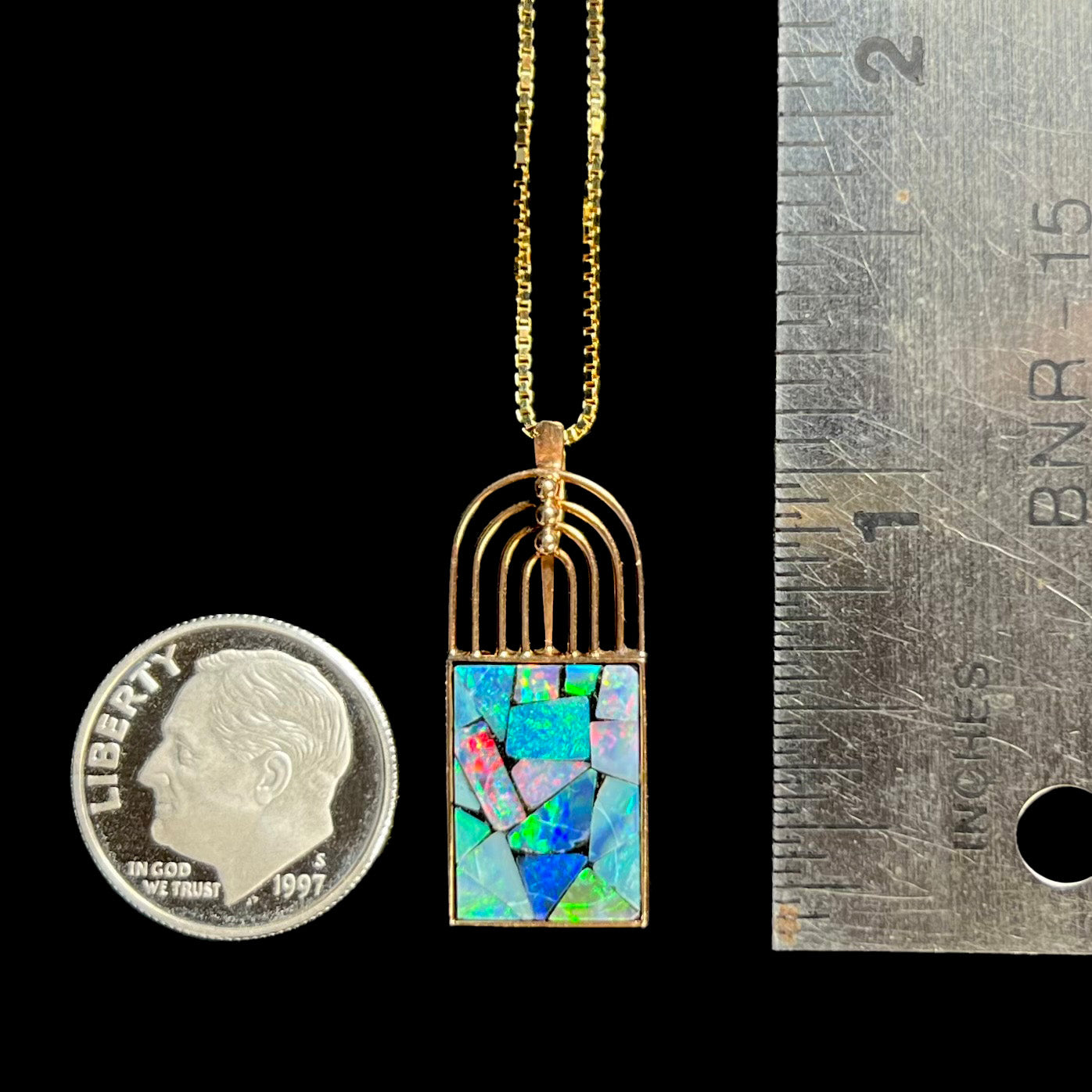 An 18k gold mosaic opal necklace placed next to a dime and ruler for scale, measuring approximately 1 inch.