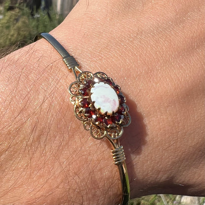 A vintage yellow gold Australian opal and garnet halo bangle bracelet shown at an angle close-up in sunlight.