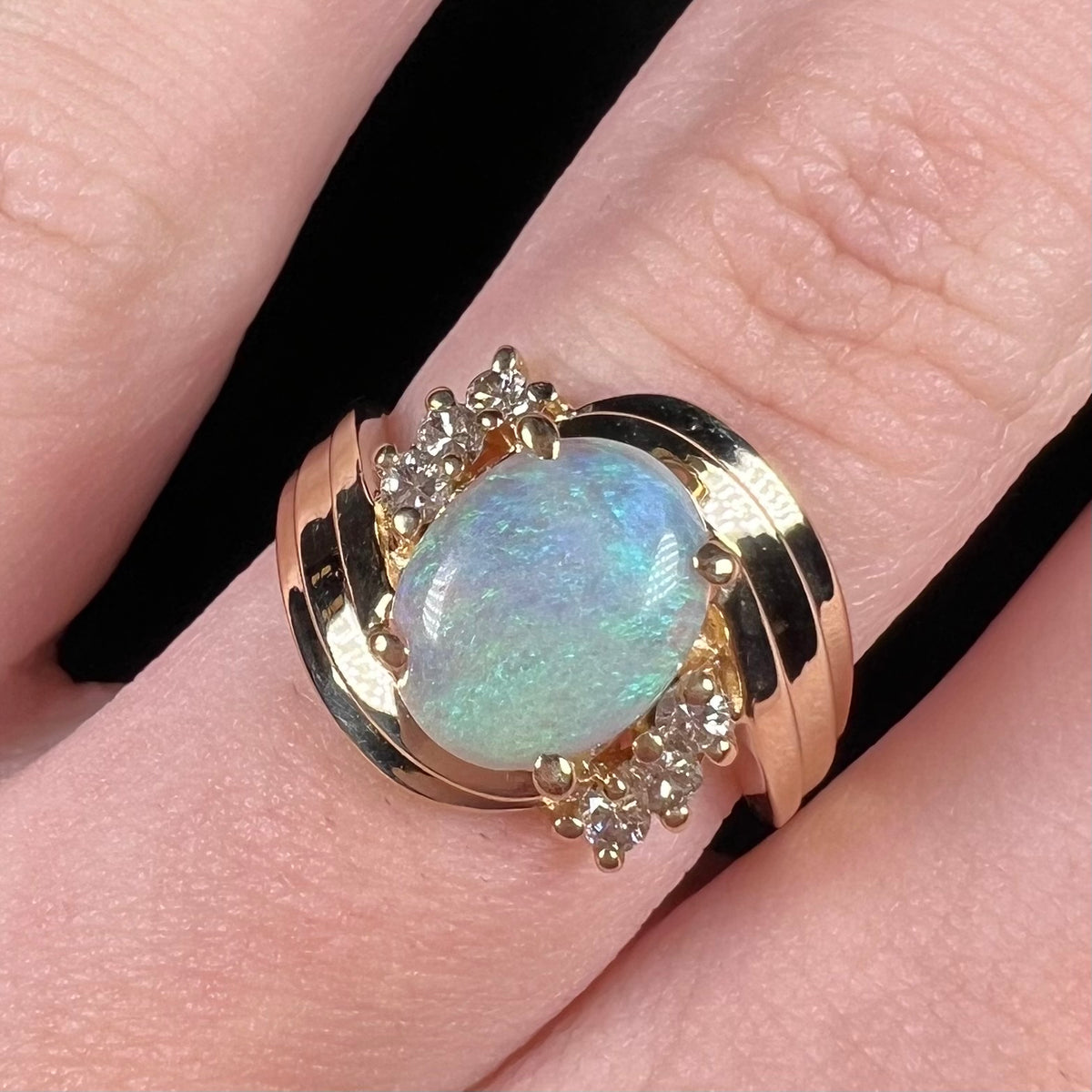 Close-up of gold opal and diamond ring with twisted bypass shank design, worn on finger