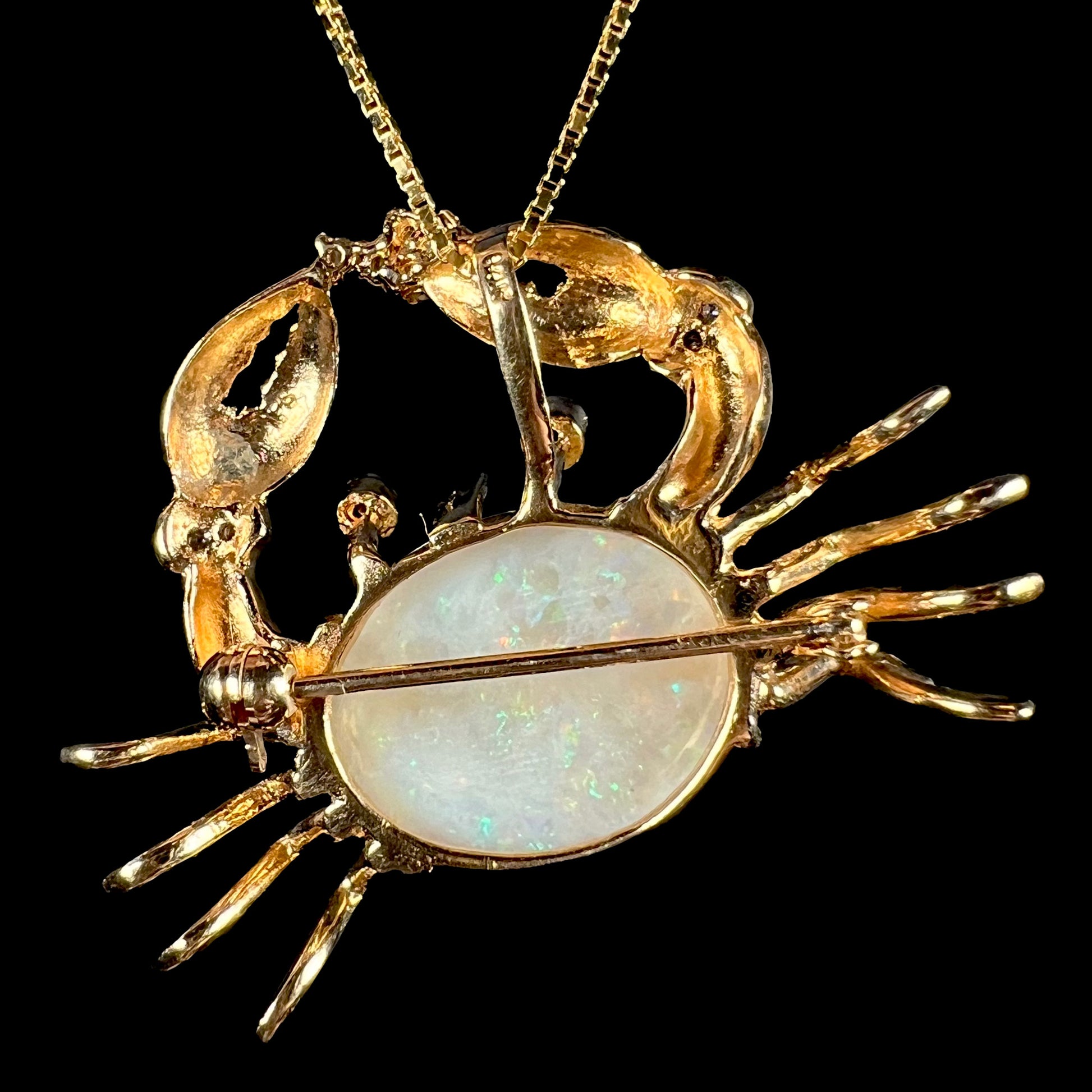 Back view of a gold opal crab brooch, showing the pin, back profile of the crab, and the underside of the opal.