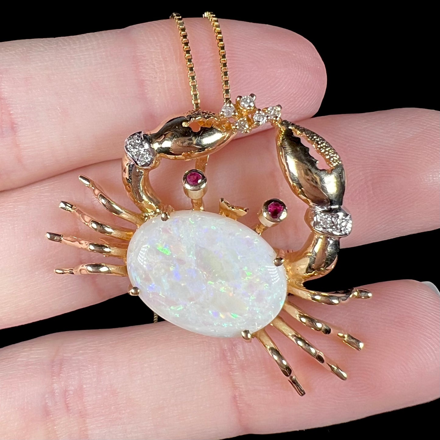 Macro view of a gold opal crab necklace resting on fingers, revealing green flashes in the opal.