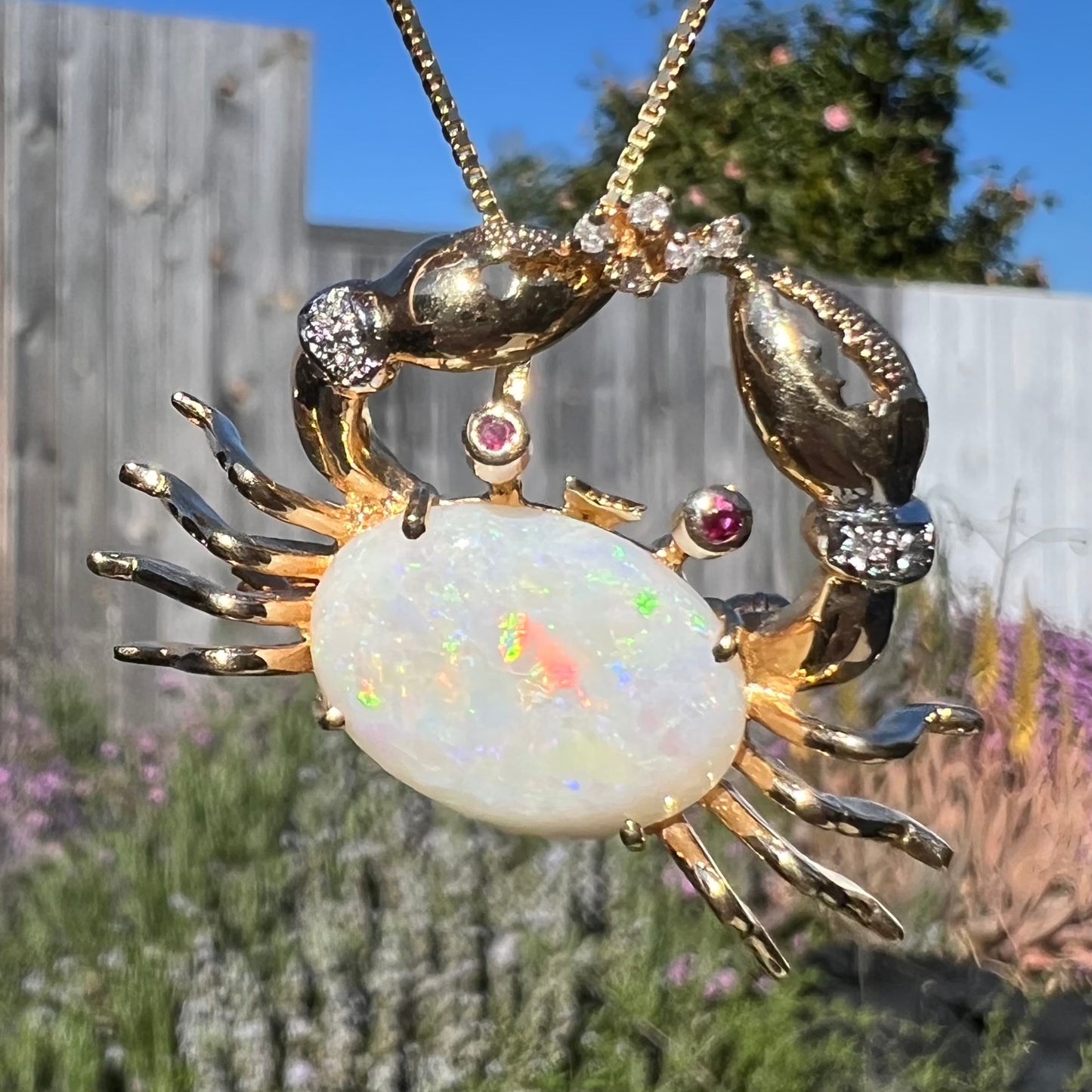 Macro view of a gold opal crab necklace in natural sunlight, showing the opal’s vibrant color play.