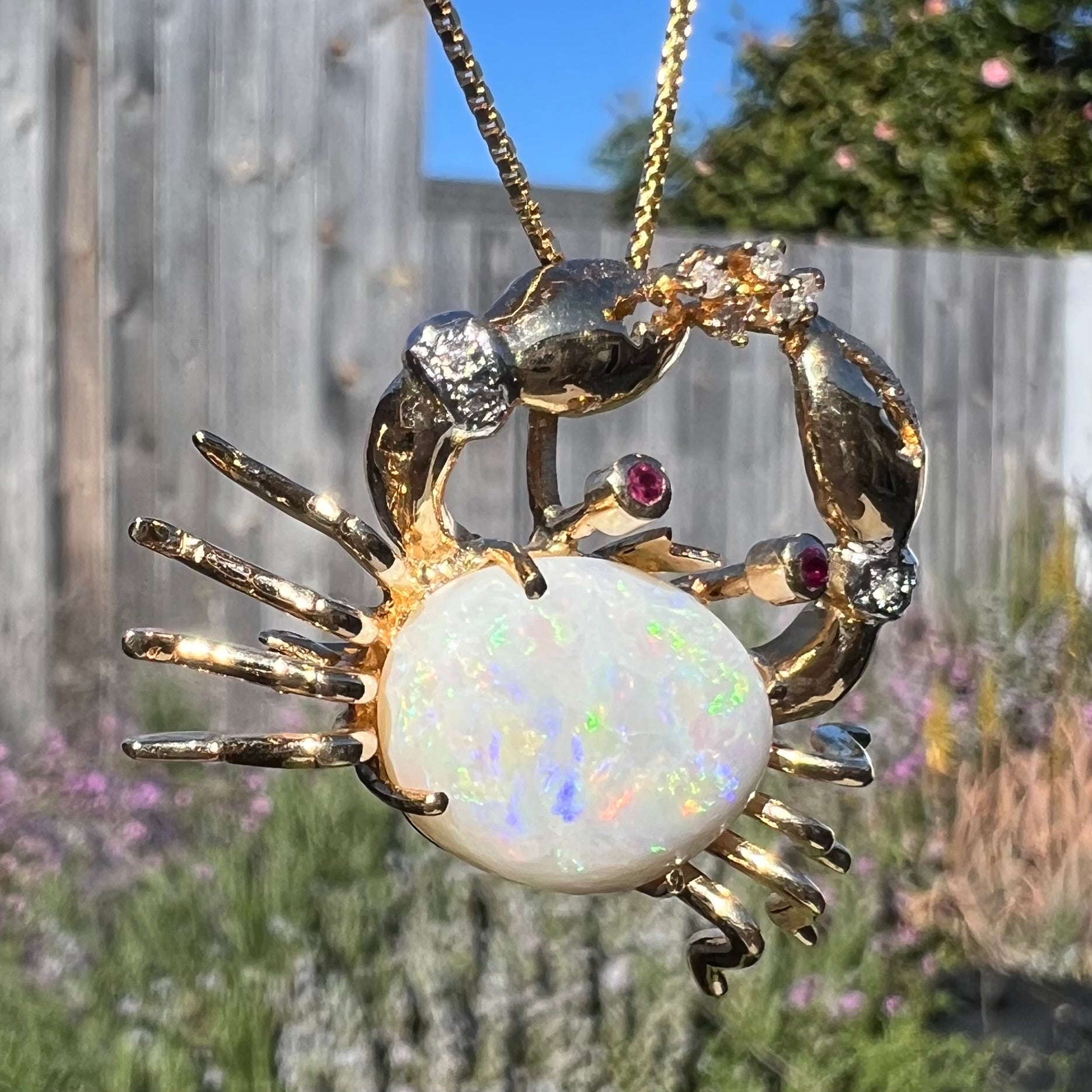 Macro close-up of a gold opal crab necklace at a twisted angle outdoors, showing blue and green flashes in the opal.