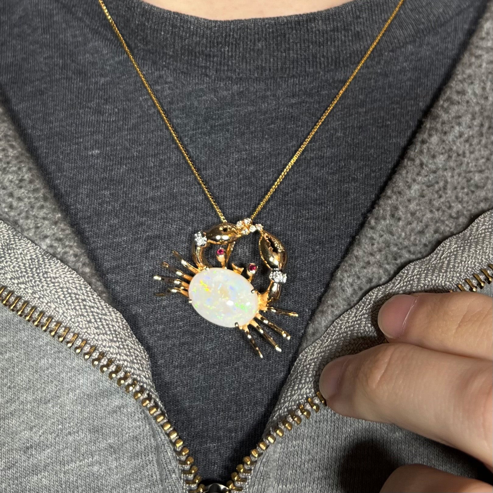 Gold opal crab necklace worn around the neck on a black t-shirt with a partially zipped sweatshirt.