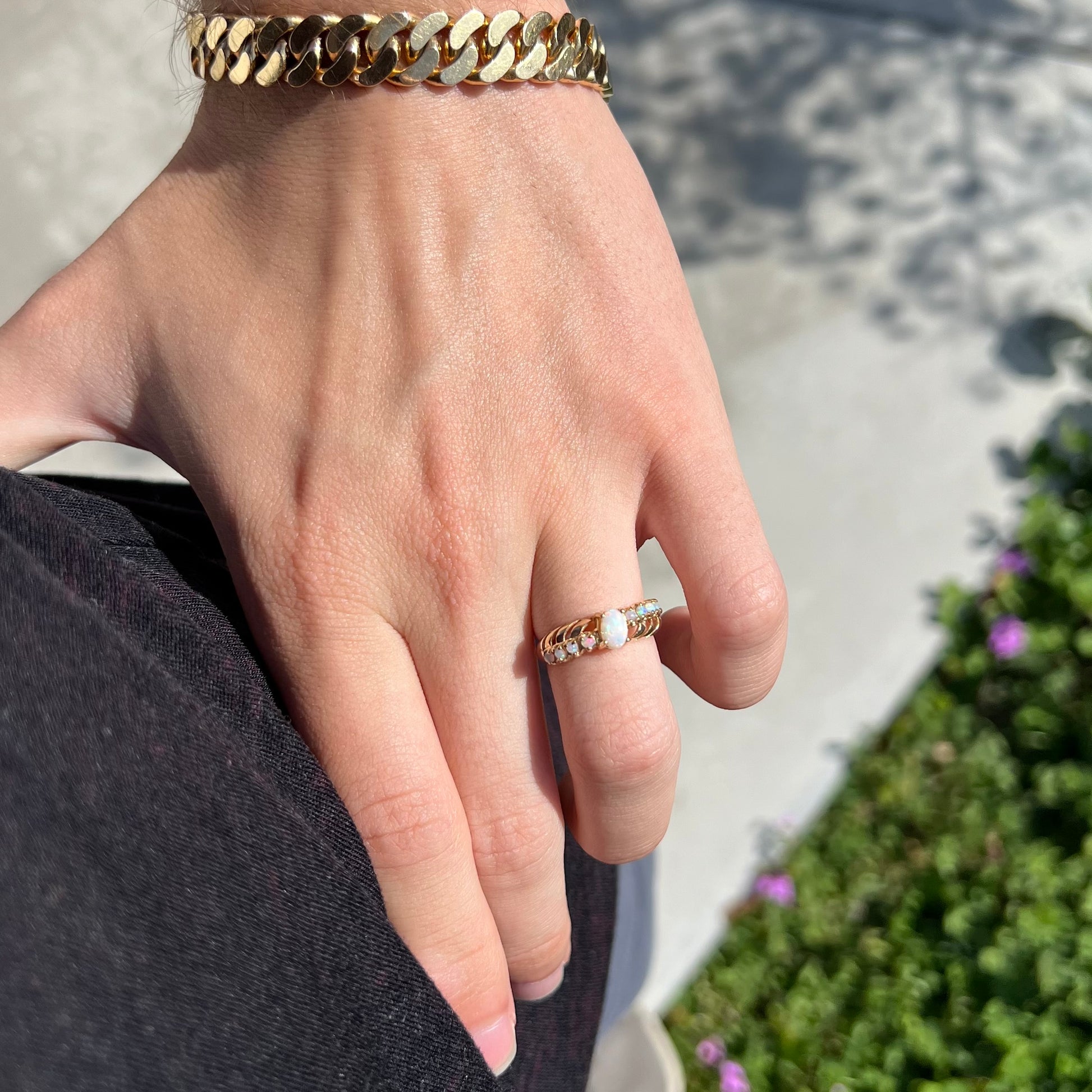 A yellow gold Australian opal crisscross ring, worn on a hand as the hand rests on the model's hip, shown in the sunlight.