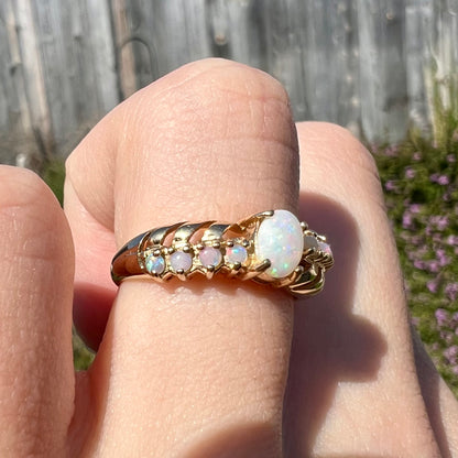 A yellow gold Australian opal crisscross ring worn on a finger, shown close-up from an angle in the sunlight.